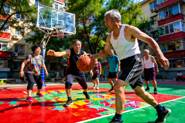 社区标准篮球场，地面涂装鲜艳，有居民正在打球