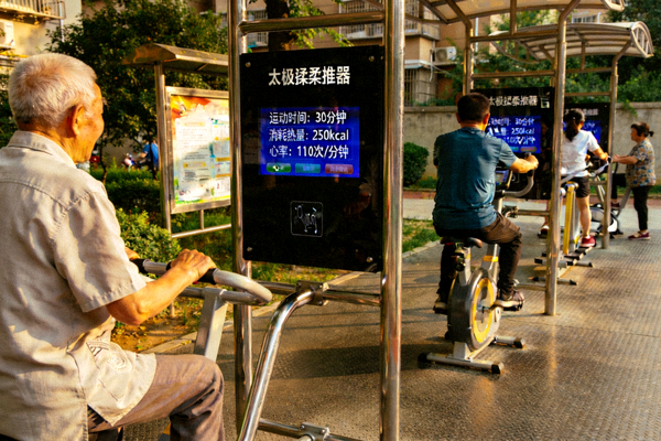 市民在社区智能健身器材区锻炼，器材屏幕显示运动数据