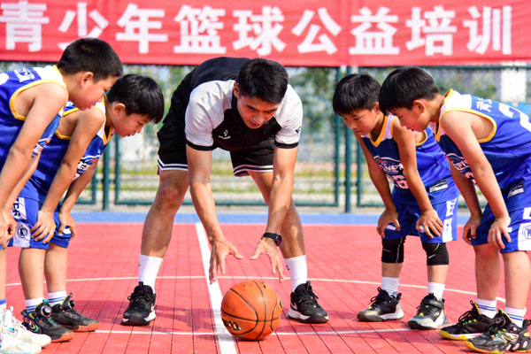 青少年篮球公益培训现场，教练正在指导孩子们进行运球练习，孩子们神情专注